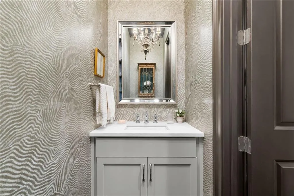 Textured wall covering featuring a wave pattern, light gray vanity cabinet, white countertop with an integrated rectangular sink, polished chrome faucet, and rectangular framed mirror