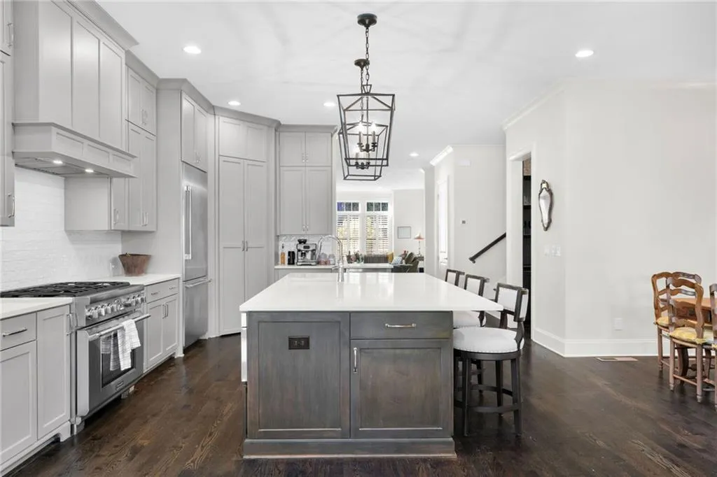Kitchen featuring shaker-style cabinetry, quartz countertops, central island with lower-cabinet storage, stainless steel gas range, and wood-finish flooring