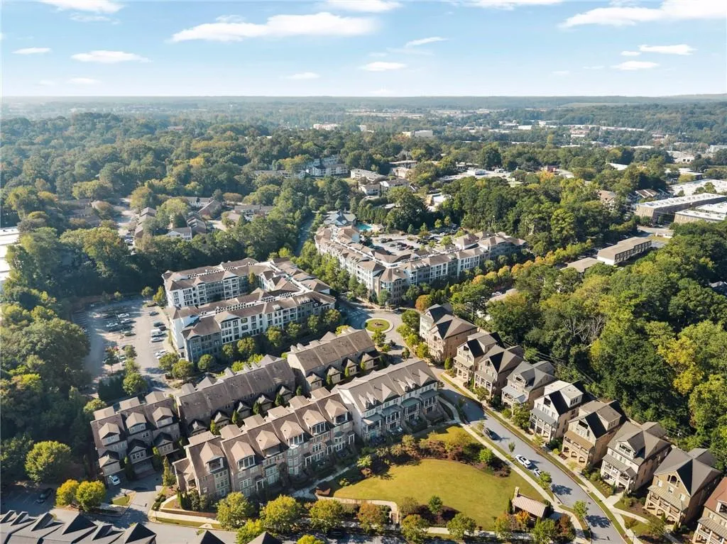 Aerial perspective of a multi-story residential complex featuring brick and stone facades, pitched roofs, surface parking areas, and mature landscaping