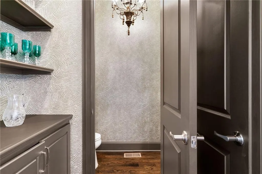 Textured wallcovering, dark wood-finish flooring, custom built-in cabinetry with open shelving, and a hanging crystal chandelier