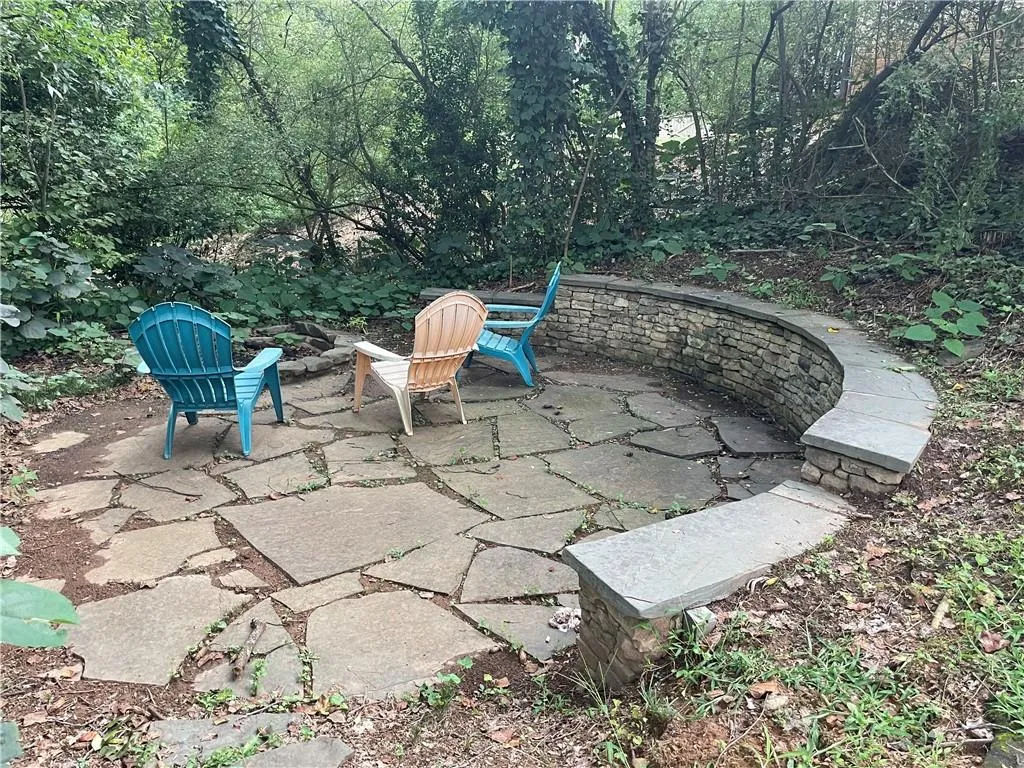 Firepit patio with stone wall. Yard is terraced with other stone walls and leads back to a small creek.