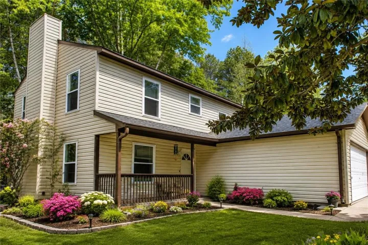 Two-story residence featuring light-toned horizontal siding, a covered front porch with a wood railing, an attached garage, and a prominent chimney