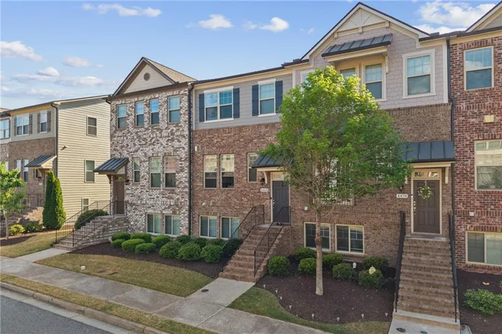 Contemporary townhome featuring a brick facade with stone accents and dark shutters