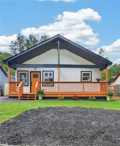 Front exterior with a covered porch, wood-tone decking, a prominent orange entry door, white siding, and a dark-pitched roofline