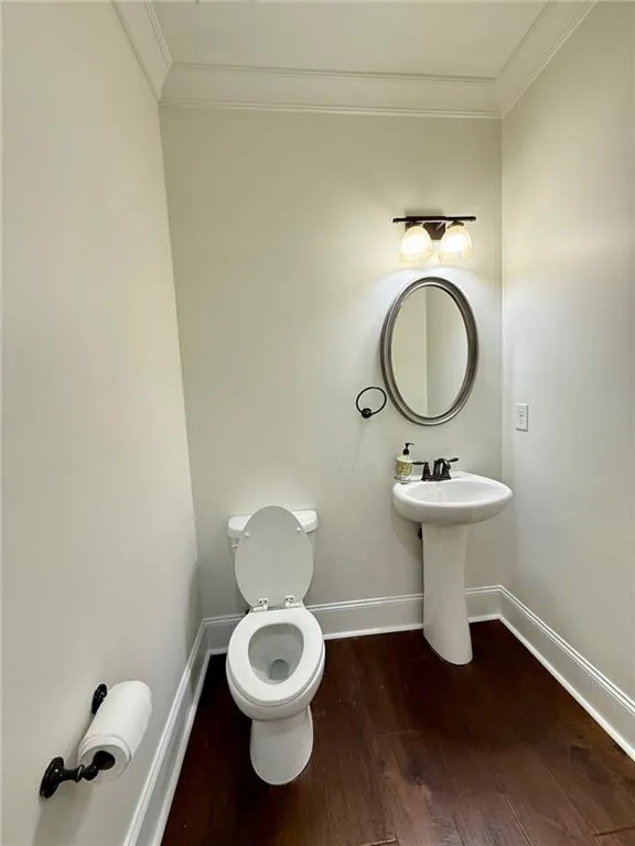 Half bath featuring crown molding and dark wood-style floors