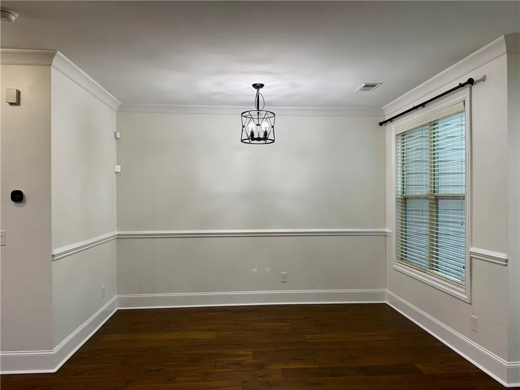 Unfurnished dining area with ornamental molding, dark wood-style floors, and a chandelier
