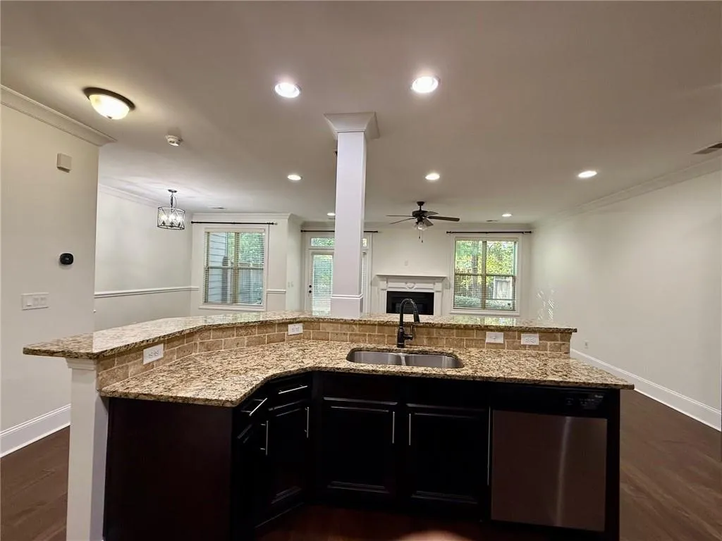 Kitchen featuring dark cabinets, dark wood-type flooring, stainless steel dishwasher, crown molding, and recessed lighting