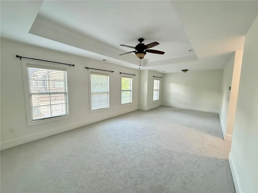 Spare room featuring a tray ceiling, light colored carpet, and a ceiling fan