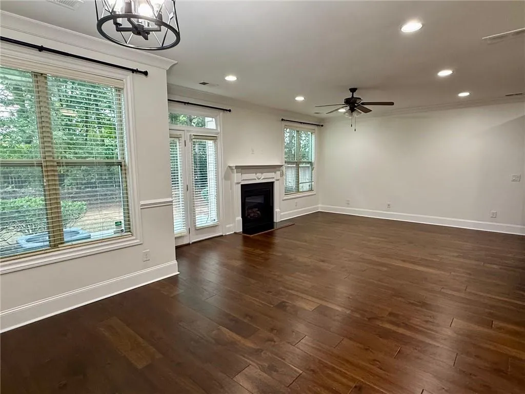 Unfurnished living room featuring recessed lighting, a fireplace with flush hearth, dark wood-style floors, ornamental molding, and a chandelier
