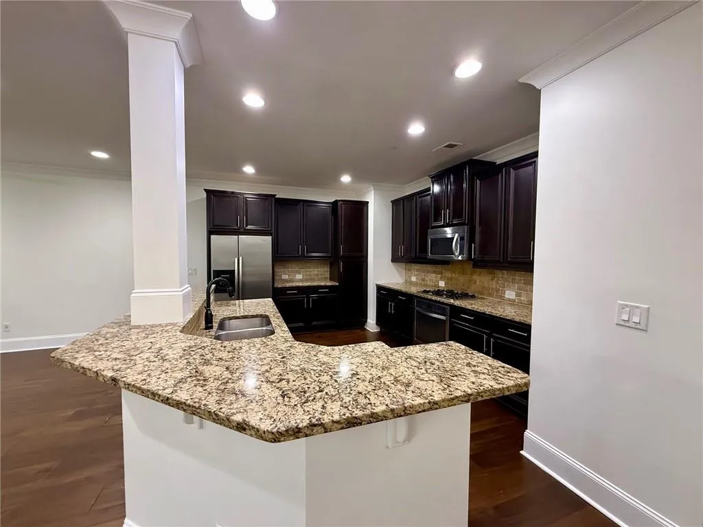 Kitchen featuring stainless steel appliances, decorative backsplash, light stone counters, dark wood finished floors, and crown molding