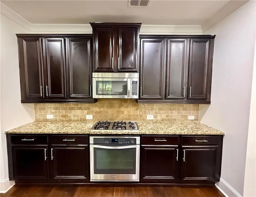 Kitchen with appliances with stainless steel finishes, dark brown cabinets, backsplash, dark wood-style flooring, and crown molding