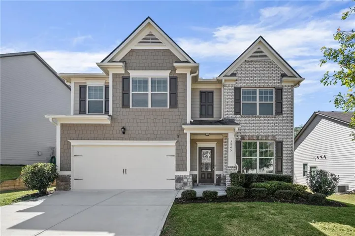 Two-story residential exterior featuring a two-car garage, brick and shingle siding, a covered entry, and manicured landscaping