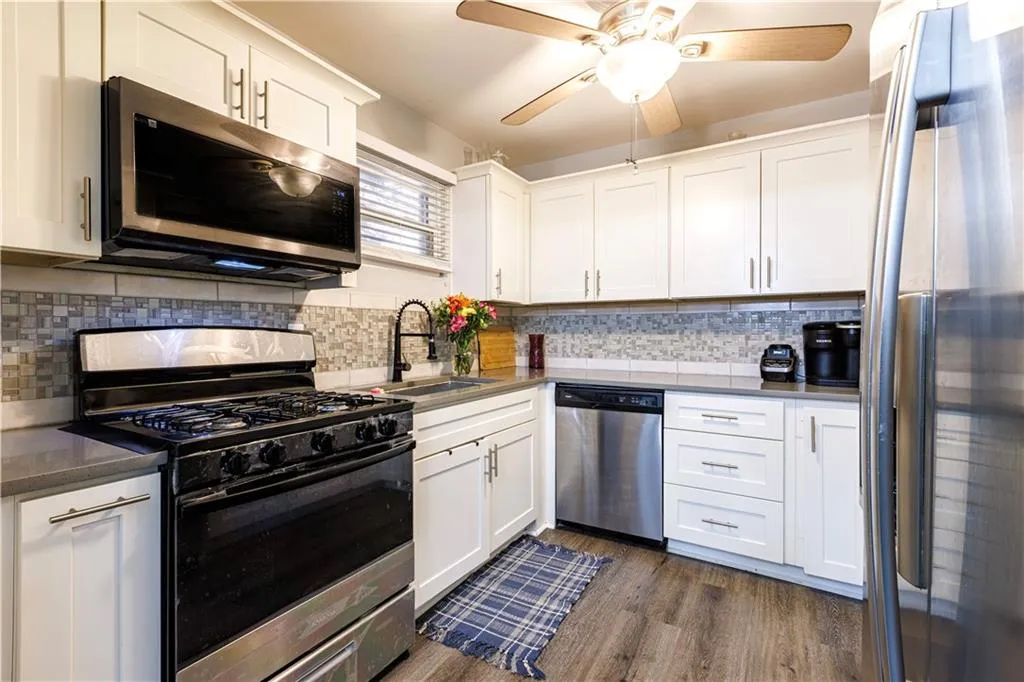 Kitchen featuring tasteful backsplash, appliances with stainless steel finishes, white cabinets, ceiling fan, and dark hardwood / wood-style flooring