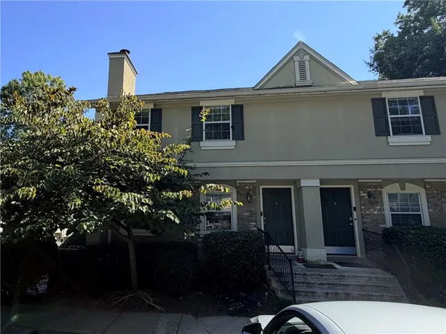 Exterior facade featuring stucco finish, multiple windows with dark shutters, dual entry doors, and a prominent chimney structure