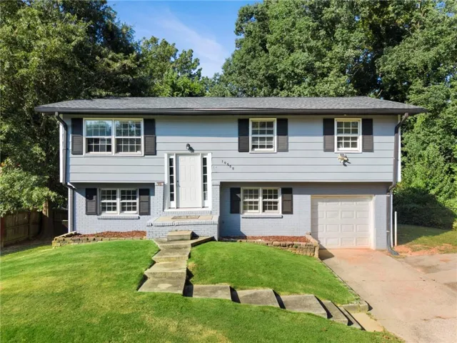 Split-level exterior featuring light gray siding, dark gray shutters, white paneled entry door, and an attached garage with a white door