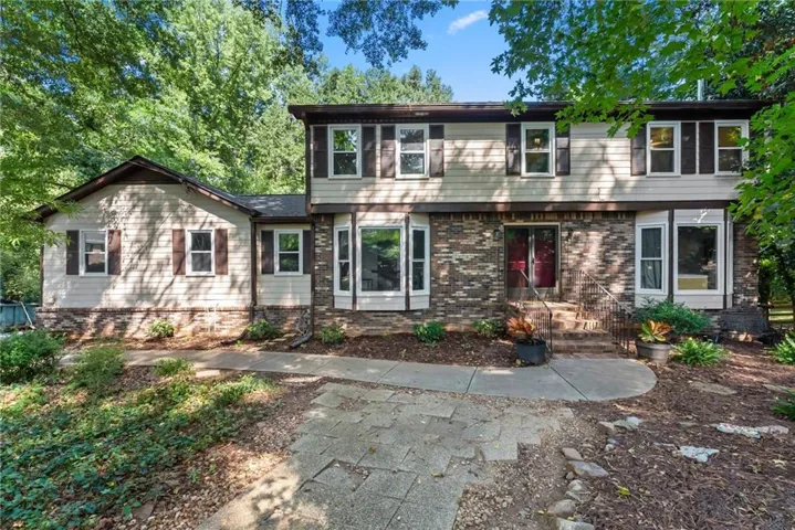 Two-story exterior with a brick and siding facade, featuring multiple bay windows, dark shutters, and a red entry door