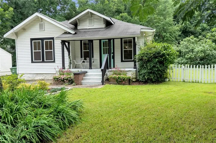White siding exterior with a contrasting black trim, covered porch, light blue front door, and a picket fence