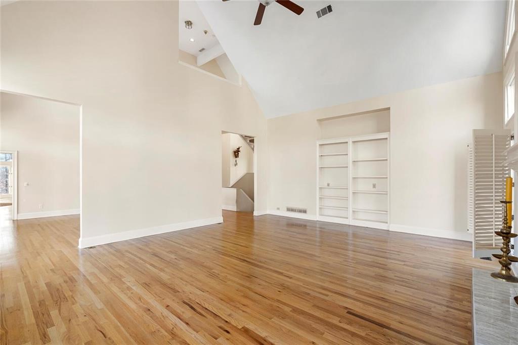 Unfurnished room with light hardwood / wood-style flooring, ceiling fan, built in features, and high vaulted ceiling