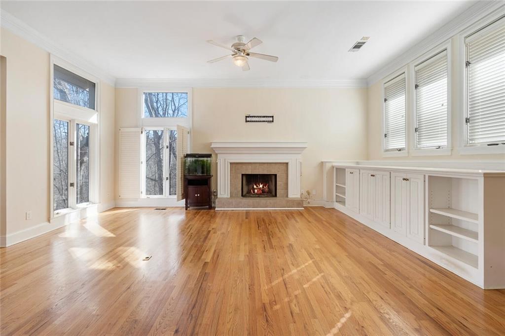 Unfurnished living room with built in features, crown molding, a tile fireplace, light wood-type flooring, and ceiling fan