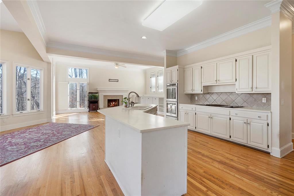 Kitchen featuring sink, light wood-type flooring, white cabinets, stainless steel double oven, and tasteful backsplash