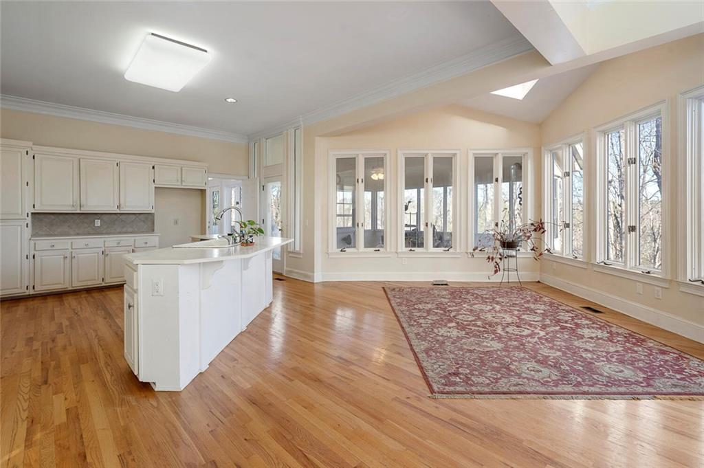 Kitchen with sink, light hardwood / wood-style floors, backsplash, a center island with sink, and white cabinetry