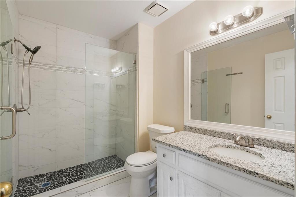 Bathroom featuring toilet, a shower with door, vanity with extensive cabinet space, and tile flooring
