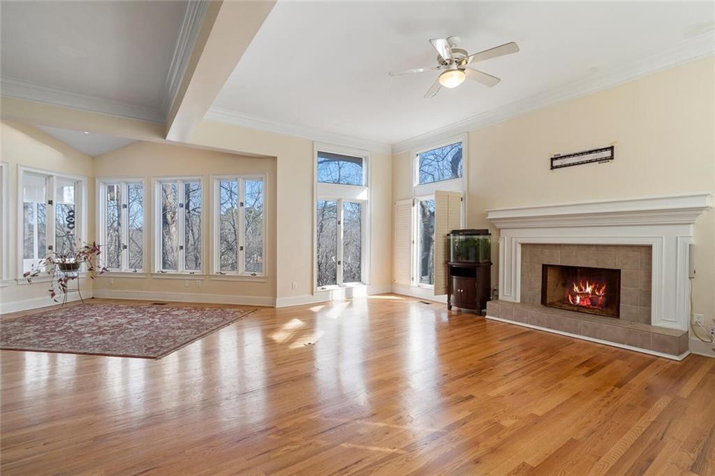 Unfurnished living room featuring a tiled fireplace, ceiling fan, light wood-type flooring, and plenty of natural light