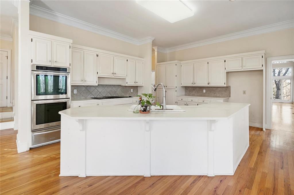 Kitchen featuring double oven, light wood-type flooring, a center island with sink, and white cabinets