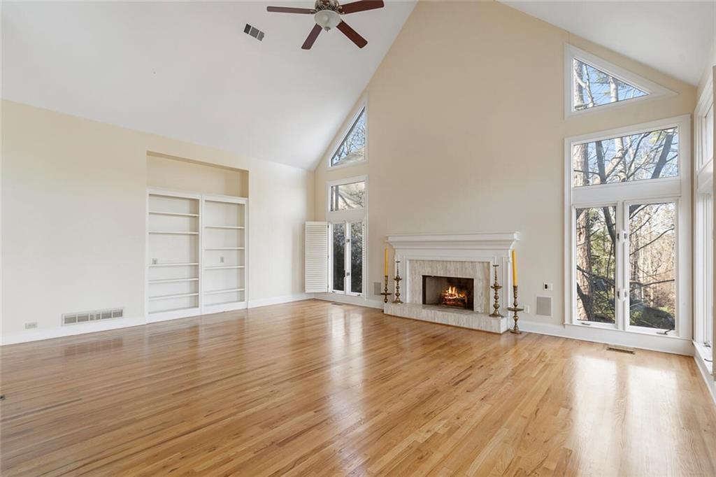 Unfurnished living room featuring ceiling fan, high vaulted ceiling, built in features, and light hardwood / wood-style floors
