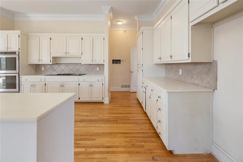 Kitchen with double oven, tasteful backsplash, ornamental molding, white cabinets, and light wood-type flooring