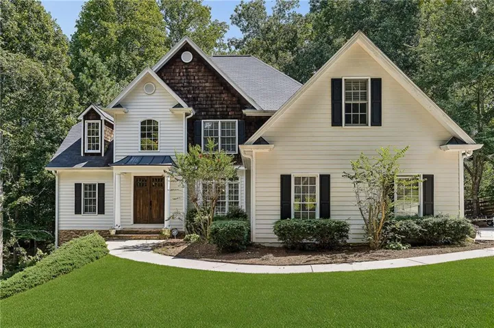 Gable rooflines with dark shingles, light siding with dark shutters, and a wood-paneled front door