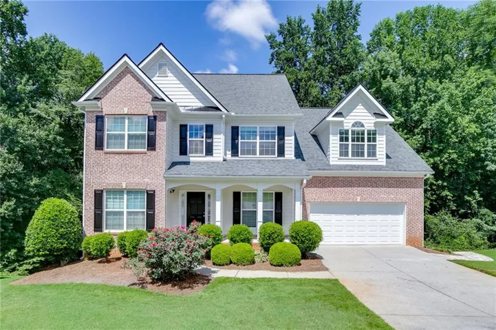 Two-story residence featuring brick and siding facade, an attached two-car garage, and a covered front porch with white columns