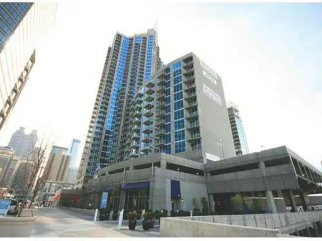 Modern high-rise residential tower featuring sleek glass and metal facade with multiple levels of expansive windows, ground-level retail and amenities space with polished concrete finishes, and contemporary architectural design integrated into an urban streetscape