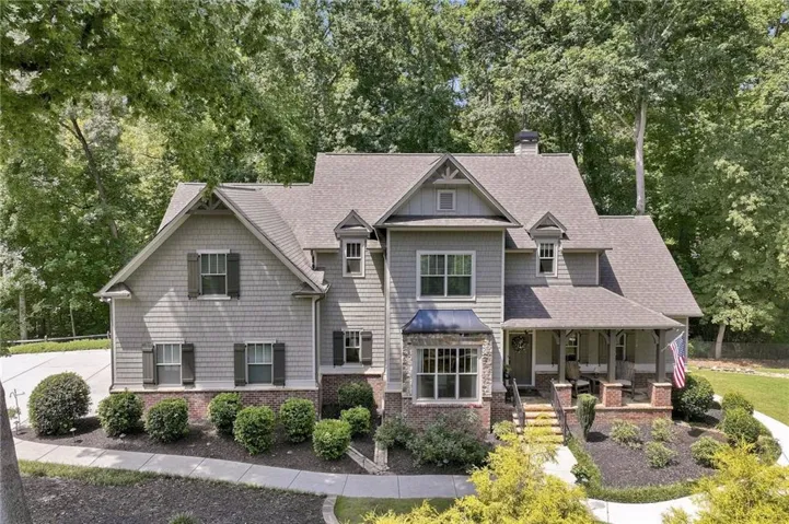 Multi-gabled residence featuring shake siding, a covered front porch with brick pillars, and mature landscaping