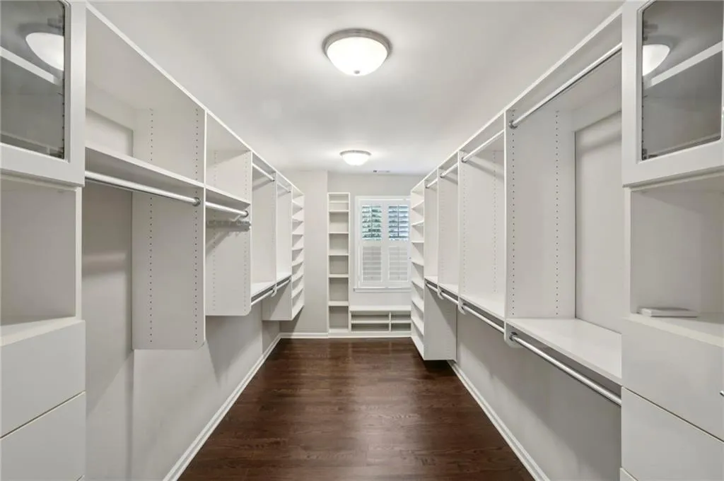 Spacious Primary Bedroom walk-in closet featuring custom built-in shelving and drawers, dark wood floors
