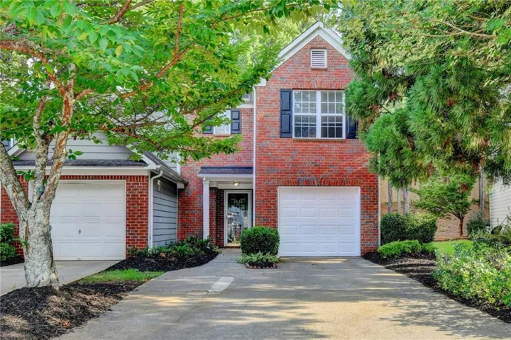 Brick facade residence featuring two white garage doors and a front entry door with a storm door