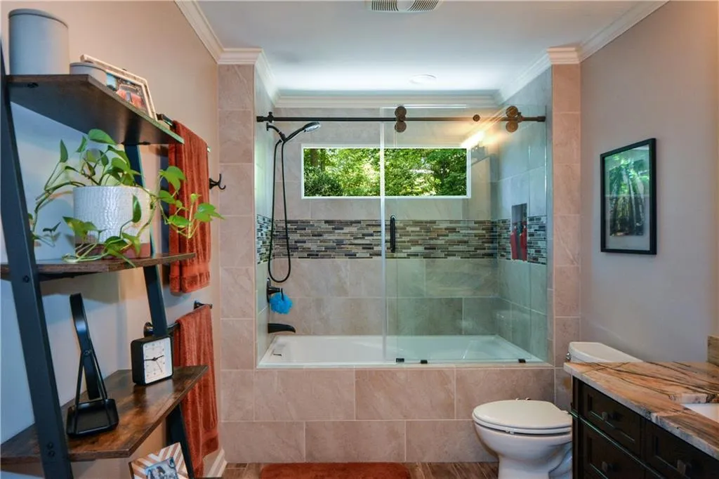 Full bathroom with crown molding, shower / bath combination with glass door, vanity, and toilet Full bathroom with crown molding, shower / bath combination with glass door, vanity, and toilet