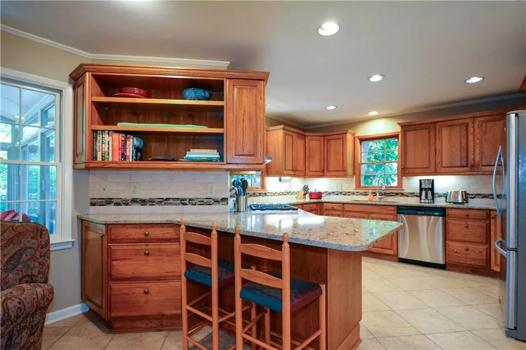 Kitchen featuring crown molding, light stone countertops, appliances with stainless steel finishes, tasteful backsplash, and light tile flooring Kitchen featuring crown molding, light stone countertops, appliances with stainless steel finishes, tasteful backsplash, and light tile flooring