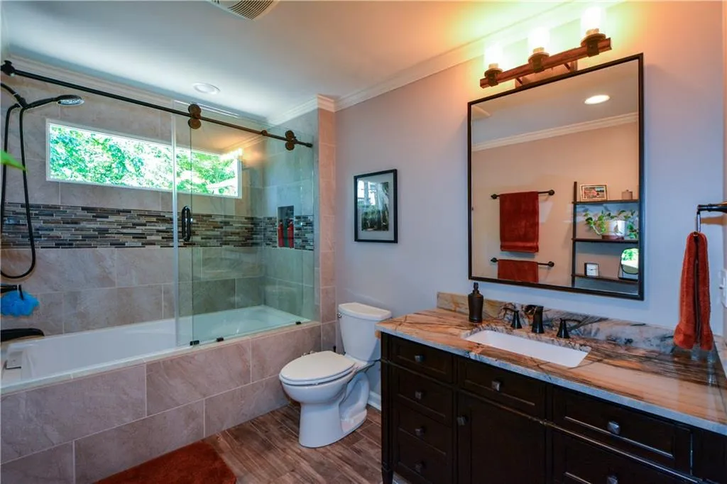 Full bathroom with combined bath / shower with glass door, oversized vanity, toilet, crown molding, and wood-type flooring Full bathroom with combined bath / shower with glass door, oversized vanity, toilet, crown molding, and wood-type flooring