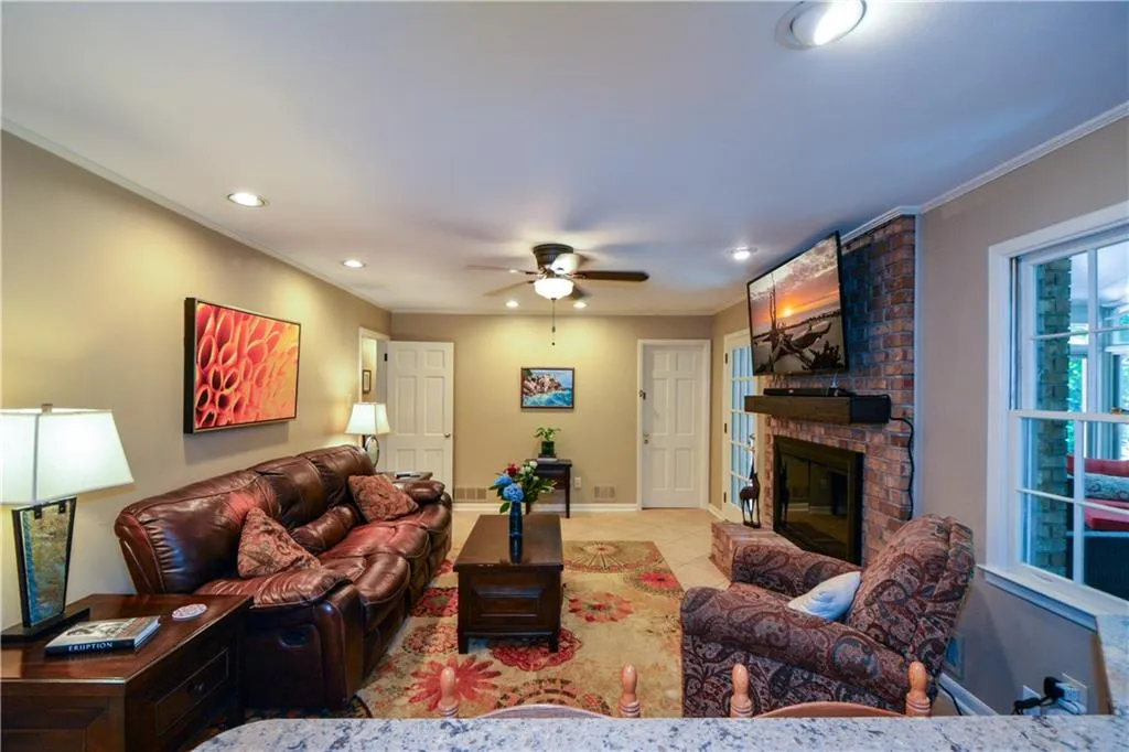 Living room featuring ceiling fan, a fireplace, light tile flooring, brick wall, and ornamental molding Living room featuring ceiling fan, a fireplace, light tile flooring, brick wall, and ornamental molding