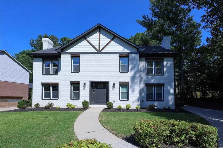 White brick exterior with black window frames, dark front door, and a concrete pathway