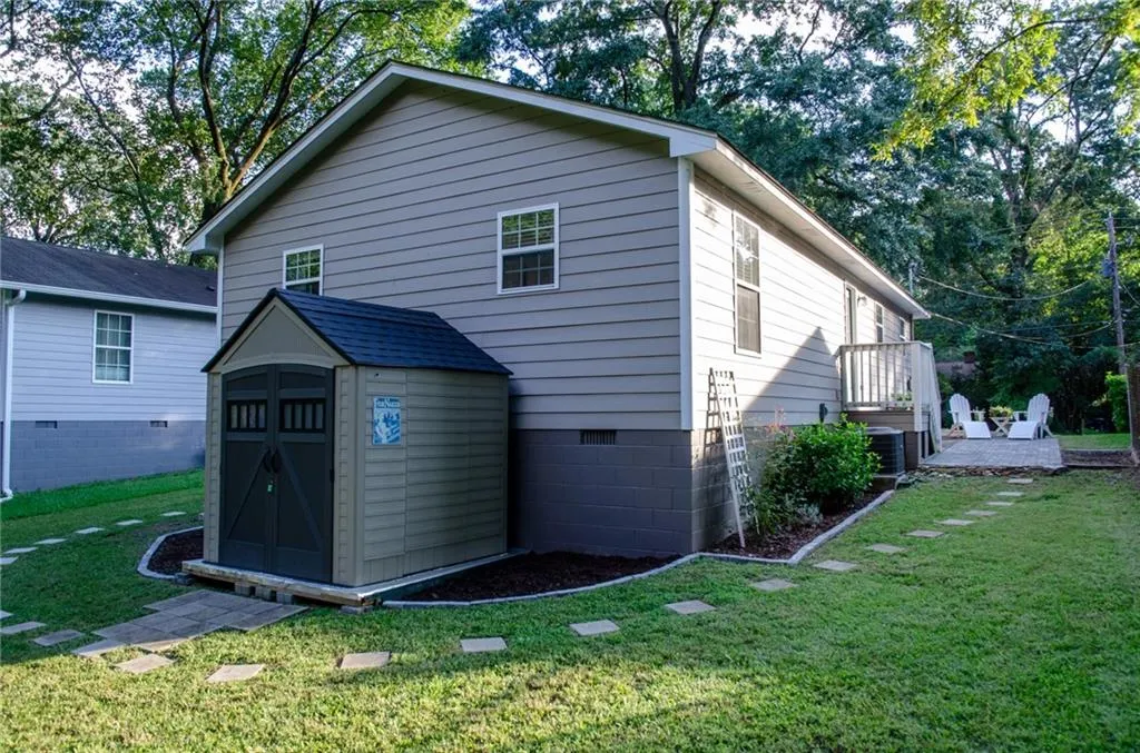 Back of house featuring crawl space, a lawn, view of wooded area, and a storage shed