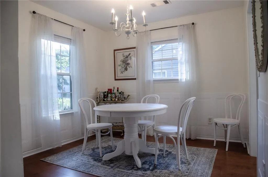 Dining space with a wainscoted wall, dark wood-type flooring, a chandelier, and a decorative wall