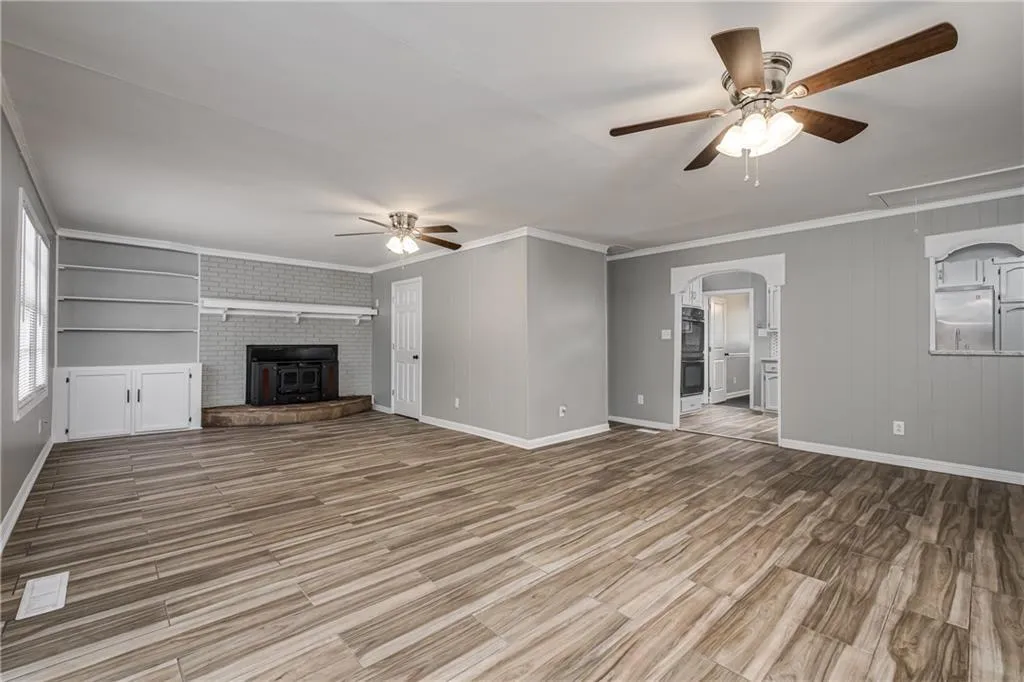 Unfurnished living room featuring ceiling fan, ornamental molding, attic access, light wood-type flooring, and wooden walls