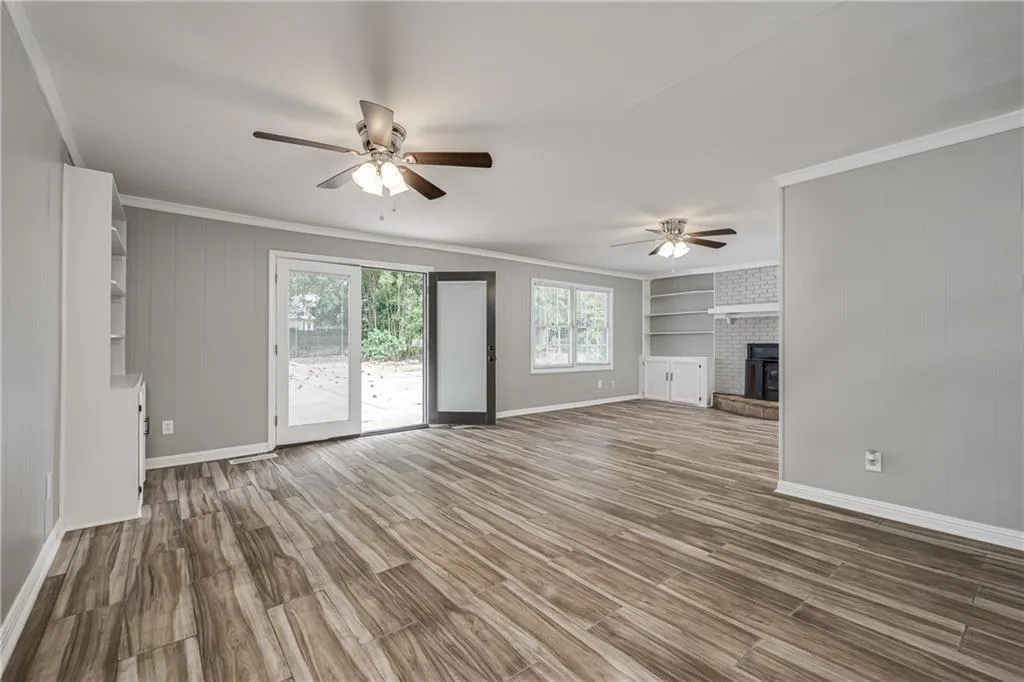 Unfurnished living room with ornamental molding, wood finished floors, a fireplace, ceiling fan, and wooden walls