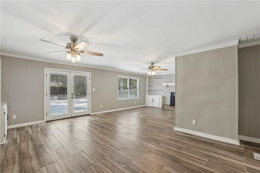 Unfurnished living room featuring french doors, a fireplace, wooden walls, crown molding, and wood finished floors