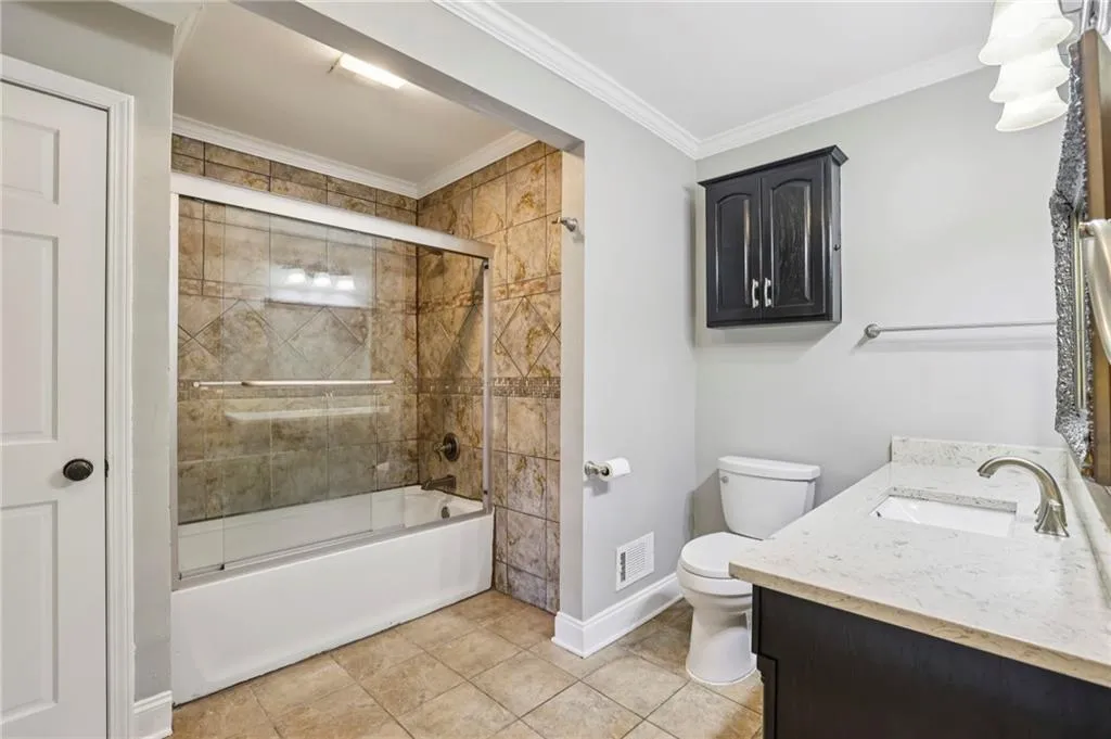 Bathroom with bath / shower combo with glass door, vanity, ornamental molding, and light tile patterned floors