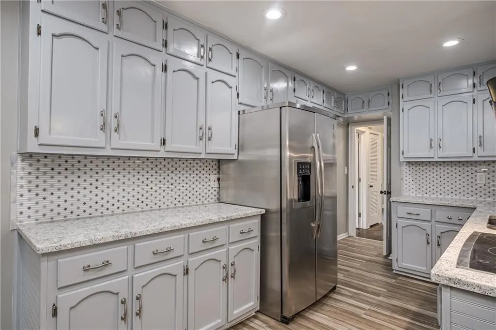 Kitchen includes plenty of cabinets, stainless steel refrigerator with ice dispenser, tiled backsplash and recessed lighting