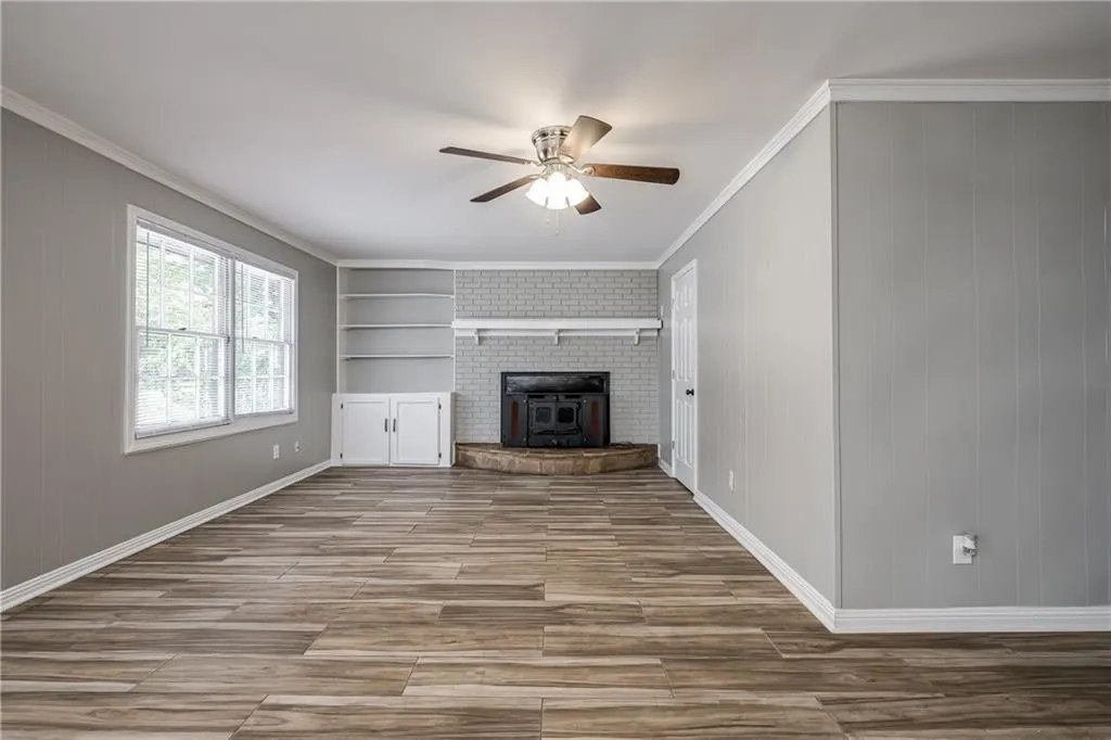 Unfurnished living room with ornamental molding, light wood finished floors, a wood stove, ceiling fan, and built in features