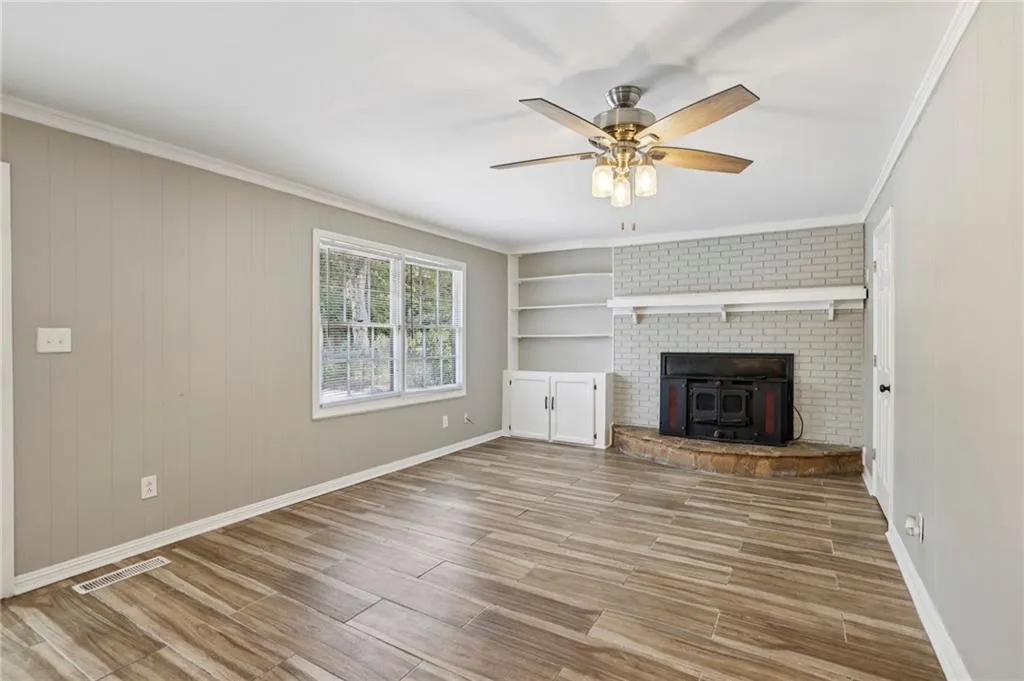 Unfurnished living room with crown molding, light wood-style flooring, ceiling fan, a wood stove, and wood walls